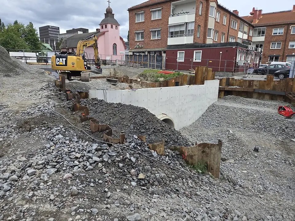 En grävplats med betongkonstruktion och en grävmaskin. "CAT" står på grävmaskinens sida.