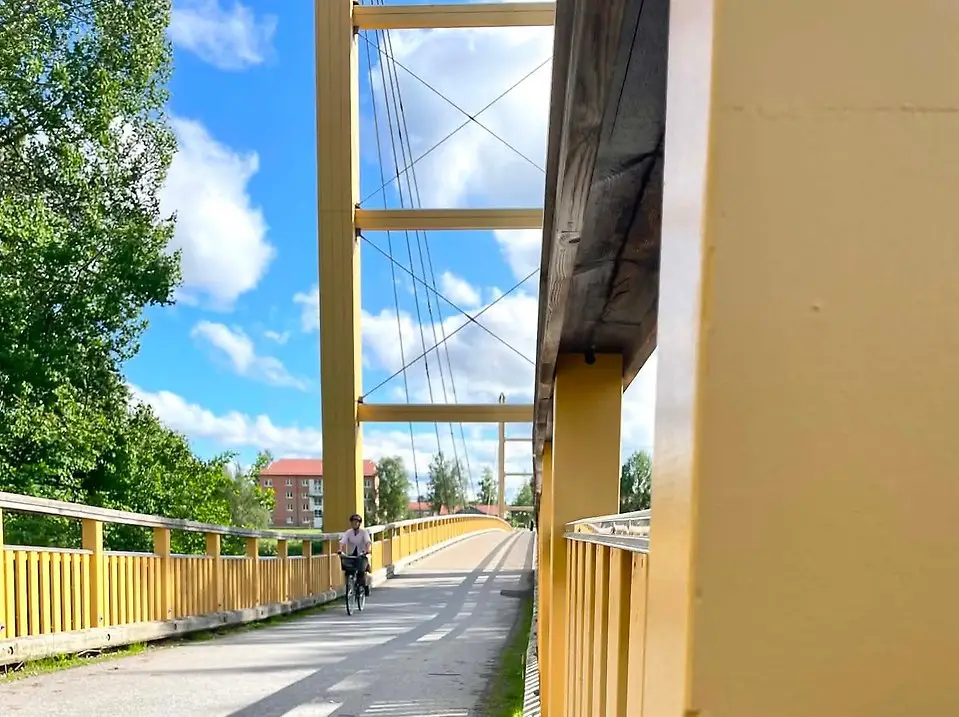 En person cyklar på en gul bro under en blå himmel med vita moln.